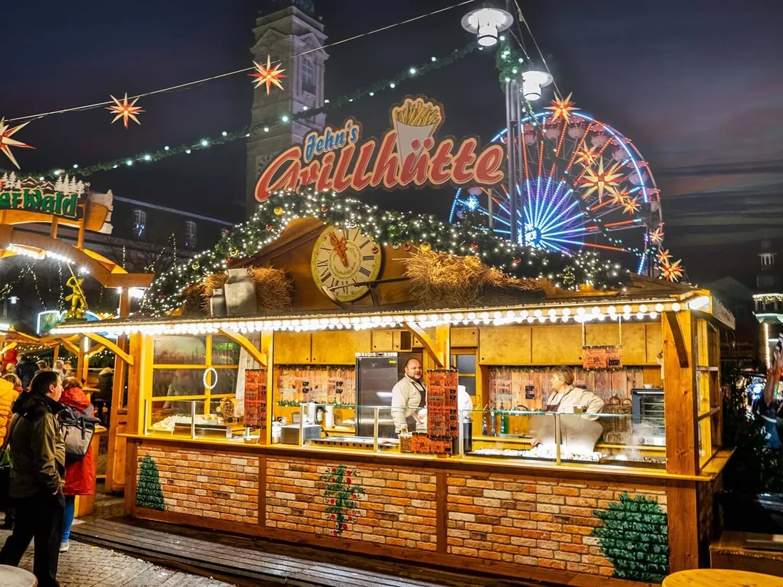 Weihnachtsmarkt mit Verkaufshütten und Riesenrad im Hintergrund