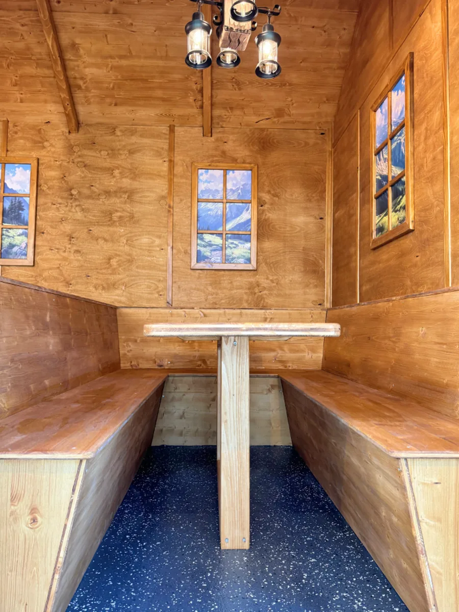 Innenraum einer Sitzhütte mit Holzbänken und festem Tisch